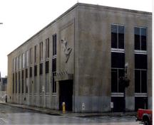 East entrance of the Government of Canada Building, showing the recessed entrance screen under a projecting stone canopy, with figurative sculpture mounted on the limestone wall, framed by a raised moulding, 1998.; Public Works and Government Services Canada / Travaux publics et Services gouvernementaux Canada, 1998.
