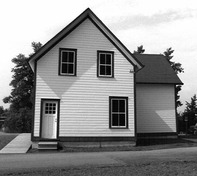 Façade du dépôt, qui montre sa forme résidentielle, avec le parement en planches à clin et le toit en croupe, 1989.; Parks Canada Agency / Agence Parcs Canada, Couture, 1989.