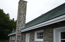 Vue de l'extérieur du pavillon de bain, qui montre les matériaux et les finis extérieurs, en particulier les assises irrégulières de pierres grossièrement taillées, les boiseries et les bardeaux en cèdre du toit.; Parks Canada Agency / Agence Parcs Canada.