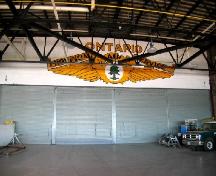 View from outside of original hangar looking at logo painted above roll-up hangar doors; City of Sault Ste. Marie
