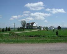 Birthplace of Roméo LeBlanc - Taken from the main street, this distant view of the house, facing west, with the elevated hillside of Memramcook East in the background; Gérard LeBlanc