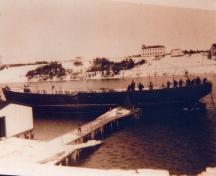 View from across the harbour of St. Gabriel's Hall, Marystown; date unknown. Building located on the crest of the hill, tower visible on the left of the building.; HFNL 2006