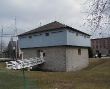 Vue en angle du Blockhaus de Merrickville montrant également les vestiges de l’ancien fossé défensif autour du bâtiment, 2004.; Parks Canada Agency / Agence Parcs Canada, 2004.