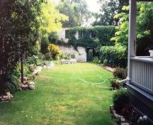 View of the side and rear yard showing the limestone wall in the background – July 1991; OHT, 1991