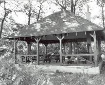 Vue générale de l'abri de pique-nique, qui montre le toit en croupe, les chevrons apparents, les poteaux de soutien en bois et les consoles en diagonale, 1992.; Parks Canada Agency / Agence Parcs Canada, 1992.