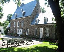 Vue générale de la maison Saint-Gabriel, qui montre le corps principal de deux étages, coiffé d’un toit incliné, dont les deux versants sont percés de petites lucarnes, de cheminées doubles et d’un clocheton, 2005.; Parks Canada Agency / Agence Parcs Canada, N. Clerk, 2005.