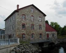 Vue latérale du vieux moulin en pierre, qui montre sa construction en maçonnerie avec ses murs extérieurs en pierre locale taillée irrégulièrement avec de massives pierres d'angle, 2004.; Parks Canada Agency / Agence Parcs Canada, 2004.