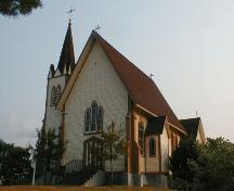 Cette image montre la charpente simple en bois de l'édifice comprenant des planches à gorge et des contreforts décoratifs en bois de style gothique ainsi que la grande tour extérieure et son clocher.; PNB 2005
