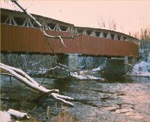 Vue de l'extérieur du pont couvert de Powerscourt, qui montre l'utilisation de planches et de lattes de parement verticales en bois.; Parks Canada Agency / Agence Parcs Canada.