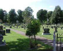 View of tombstones, the cemetery cross and the chapel in the background; Memramcook Valley Historical Society