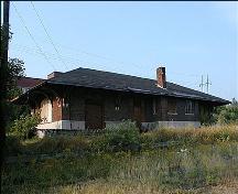 Cette image montre le toit en croupe de bardeaux d’asphalte noir qui a un large débordement soutenu par des consoles décoratives reposant sur des appuis en granit fixés aux murs de briques.; PNB 2005