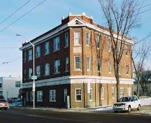 This image illustrates the overall form and massing of the building, in its prominent corner location. Also shown are the three levels of residential uses and a prominent corner facade with parapet and pediment above the third floor window. ; City of Edmonton, 2004