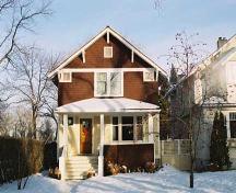 This image illustrates the two storey south wood-clad facades with front  gable, soffit support brackets, corner 'eye' windows and full-width hipped-roof veranda.; City of Edmonton
