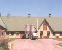 La façade sud de l'Édifice de l'exposition permanente du porc, no 91, qui montre le toit utilitaire à deux versants en pente moyenne avec les grandes lucarnes et les ventilateurs de toit, 1995.; Agence Parcs Canada / Parks Canada Agency, Cosimo Zacconi, 1995.