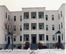 View of the façade of Building 23, showing the projecting balconies over the principal entrance, the central pavilion stair bays and the entrance court porches, 1994.; Department of National Defence / Ministère de la Défense nationale, 1994.