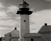 View of the Lighthouse, showing the simple massing, which consists of a white, concrete, hexagonal tower, a hexagonal concrete gallery and a red iron lantern, 1987.; Ministère des Transports / Department of Transport, 1987.