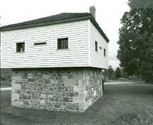 Vue en angle du blockhaus, qui montre la volumétrie carrée sur deux étages, le toit pyramidal et la cheminée, 1989.; Department of Public Works / Ministère des Travaux publics, 1989.