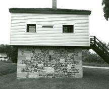 Façade latérale du blockhaus, qui montre le rez-de-chaussée en maçonnerie de pierre et l’étage à charpente en bois couverte d’un parement de planches à clins, 1989.; Department of Public Works / Ministère des Travaux publics, 1989.