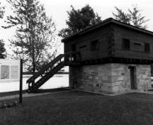 Vue en angle du blockhaus, qui montre la volumétrie carrée sur deux étages et le toit pyramidal, 1989.; Department of Public Works / Ministère des Travaux publics, 1989.