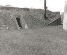Vue de la poudrière de l'est, qui montre le volume bas et discret, partiellement souterrain, de ces structures en brique rectangulaires renforcées en brique, 1989.; Parks Canada Agency / Agence Parcs Canada, 1989.