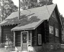 Rear view of the Gate Keeper's Residence, showing the rectangular plan, with a projecting front porch to the right and a shingled, gable roof with one chimney, 1984.; Parks Canada Agency / Agence Parcs Canada, S. Siepman, 1984.