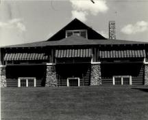 General view of the Golf Clubhouse (B7), showing the horizontal log construction and the cobblestone detailing, 1984.; Agence Parcs Canada / Parks Canada Agency, 1984.