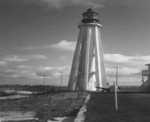 Vue générale du phare, qui montre les huit arcs-boutants en béton à motif palmé qui soutiennent la structure à chacun des trois niveaux principaux, 1990.; Parks Canada Agency / Agence Parcs Canada, 1990.