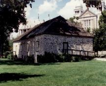 Vue de l’entrepôt de la Baie d’Hudson, qui montre son toit en croupe bas percé de lucarnes.; Agence Parcs Canada / Parks Canada Agency.