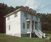 Vue de la façade générale du bâtiment 49, qui montre le volume sur deux étages, avec le toit en croupe et les lucarnes, vers 2004.; Parks Canada Agency / Agence Parcs Canada, circa/vers 2004.
