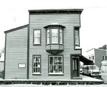 Side view of Mme. Tremblay's Store, showing the inset and splayed corner window, and the oriel window, 1987.; Department of the Environment / Ministère de l'Environnement, 1987.