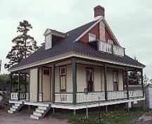 Vue générale du bâtiment 34, qui montre la grande véranda qui ceinture la maison, les consoles en bois et les balustres chantournées de la véranda, vers 2004.; Parks Canada Agency / Agence Parcs Canada, circa / vers 2004.