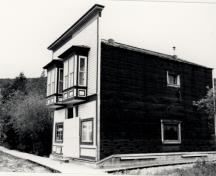 General view of Ruby's Place, showing the horizontal, painted, coved siding of the street façade with its distinctive, large oriel windows, 1987.; Parks Canada Agency / Agence Parcs Canada, 1987.