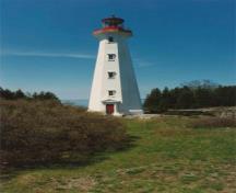 Vue générale du tour de la station de phare, qui montre la volumétrie simple, soit un bâtiment octogonal effilé coiffé d’une lanterne proéminente, et les fenêtres à six carreaux sur les quatre niveaux, 1990.; Department of Transport / Ministère des Transports, 1990.