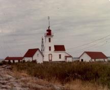 Side view of the Lighthouse and Dwelling on Gereaux Island, showing the three-storey, square, tapered form of the tower and the attached gable-roofed dwelling that is well integrated with the tower, 1981.; Parks Canada Agency / Agence Parcs Canada, 1981.