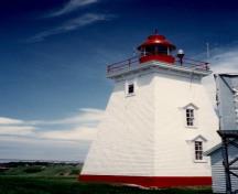 Vue générale du phare, qui montre le profil simple, avec la lanterne octogonale proéminente dont les proportions s’accordent avec celles de la tour, et le garde-fou de la galerie, vers 1990.; Transport Canada / Transports Canada, circa / vers 1990.