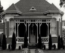 Façade du bâtiment 20, qui montre la porte d’entrée double à l’avant, la véranda avec ses boiseries décoratives et la main courante, 1988.; Department of National Defence / Ministère de la Défense nationale, 1988.