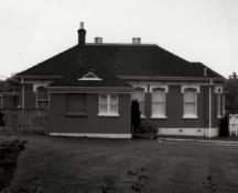 Vue de la façade latérale du bâtiment 20, qui montre le volume bas de ce bâtiment rectangulaire en brique d’un étage, coiffé d’un toit en croupe, 1989.; Parks Canada Agency / Agence Parcs Canada, 1989.