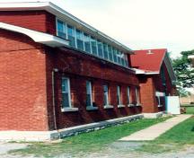 View of the side façade of RMC Building 36, showing the stone base typical to the buildings of the immediate complex and other structures nearby, 1993.; Parks Canada Agency / Agence Parcs Canada, 1993.