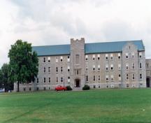 Vue générale du bâtiment 31 du CMR, qui montre la disposition régulière des fenêtres, la ligne de toiture continue et la tour centrale carrée, 1993.; Department of National Defence / Ministère de la Défense nationale, 1993.
