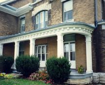 View of the front porch of the RMC Building 27, showing the large panelled-box posts and large dentils on the eaves, 1993.; Parks Canada Agency / Agence Parcs Canada, 1993.