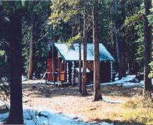 Corner view of the Sandhills Warden Cabin, showing the rectangular plan, and gabled roof clad in cedar-shingles, 1996.; Agence Parcs Canada / Parks Canada Agency, 1996.