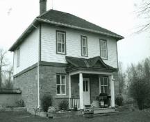 Façade de la résidence fortifiée du maître-éclusier, qui montre la volumétrie sur deux étages, le toit en croupe, et la cheminée, 1989.; Parks Canada Agency / Agence Parcs Canada, Couture, 1989.
