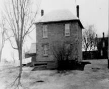 Vue de la façade est de la maison fortifiée du maître-éclusier, qui montre l’agencement symétrique des fenêtres de l’étage, 1930.; Parks Canada Agency / Agence Parcs Canada, 1930