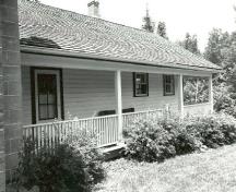 Façade of the Defensible Lockmaster's House, showing the single-storey clapboard addition with full-length verandah, 1989.; Parks Canada Agency / Agence Parcs Canada, Couture, 1989.