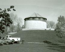 Vue générale de la tour Martello Murney, qui montre son profil et sa volumétrie, soit une tour circulaire reposant sur un parapet, 1991.; Parks Canada Agency / Agence Parcs Canada, Fern Graham, 1991.