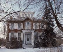 View of the main façade of Bentley House, showing the centre door accentuated by a delicate porch, supported by delicate Italian colonnettes, 1992.; Public Works and Government Services Canada / Travaux publics et Services gouvernementaux Canada, 1992.