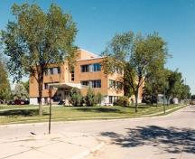 Vue en angle du bâtiment 84, où l'on peut apercevoir sa volumétrie basse et horizontale, et ses portiques en saillie d’aspect uni, 1996.; Department of National Defence / Ministère de la Défense nationale, 1996.