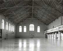Vue du Manège militaire, qui montre le grand espace intérieur de la salle d’exercices enjambé par des fermes Fink, et la galerie qui court sur toute la longueur de la salle, 1992.; Ministère de la Défense nationale / Department of National Defence, 1992