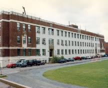 Vue de la façade principale de l’édifice Currie, S37, qui montre les angles en retrait qui créent l’illusion d’un pavillon central flanqué d’ailes latérales, 1997.; Heritage Canada/ Patrimoine canadien, 1997.