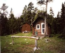 Front elevation of the Fourtpoint Warden Cabin, showing the upper course extension forming a small porch overhang and the red-brown exterior paint with light trim, 1996.; Parks Canada Agency / Agence Parcs Canada, 1996.